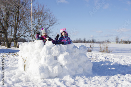 Girls standing in large snow fort with snowballs