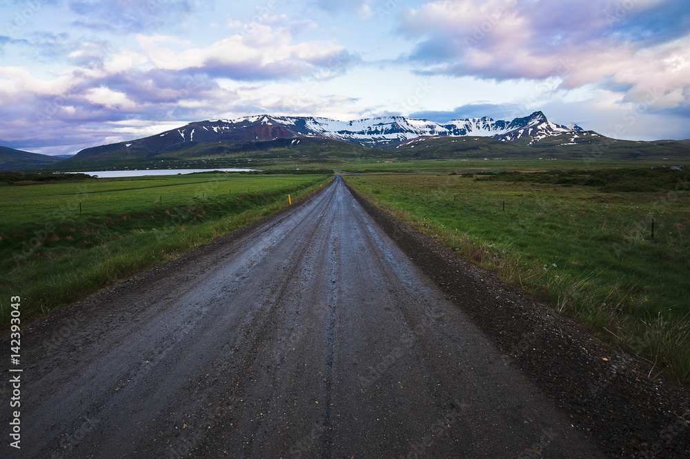 Travel postcard from Iceland with a dirt road and snow mountains early morning