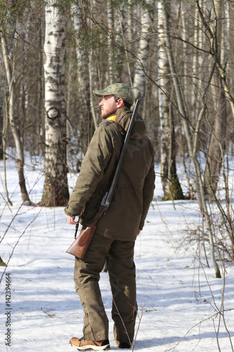 Hunter man with old 16 caliber side-by-side double-barreled shotgun dressed in dark khaki clothing in the forest © joppo