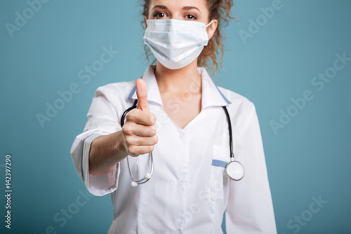 Confident doctor or nurse wearing surgical mask and showing thumbs-up