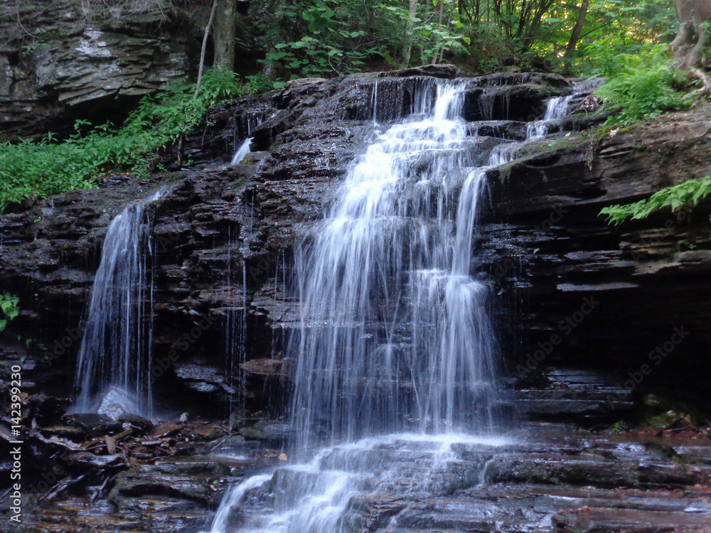 Fototapeta premium Scenic little waterfall flowing over a high rocky mound.