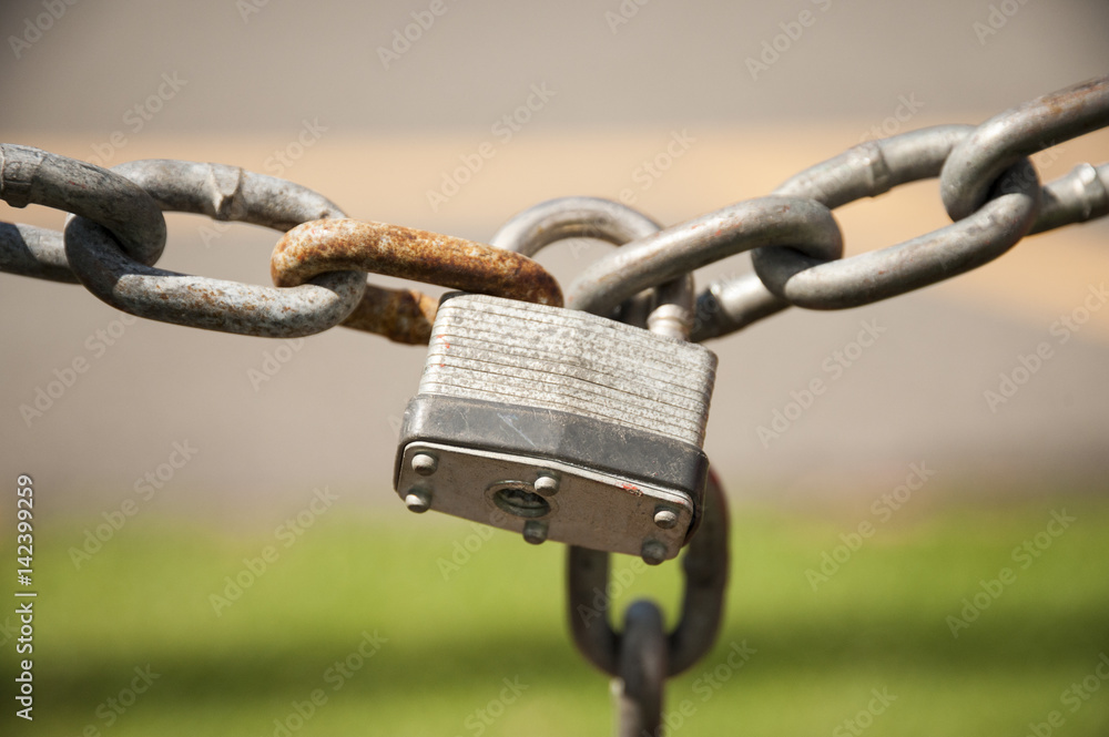 An old padlock linking two rusty chains with an out of focus background An old padlock linking two rusty chains with an out of focus background