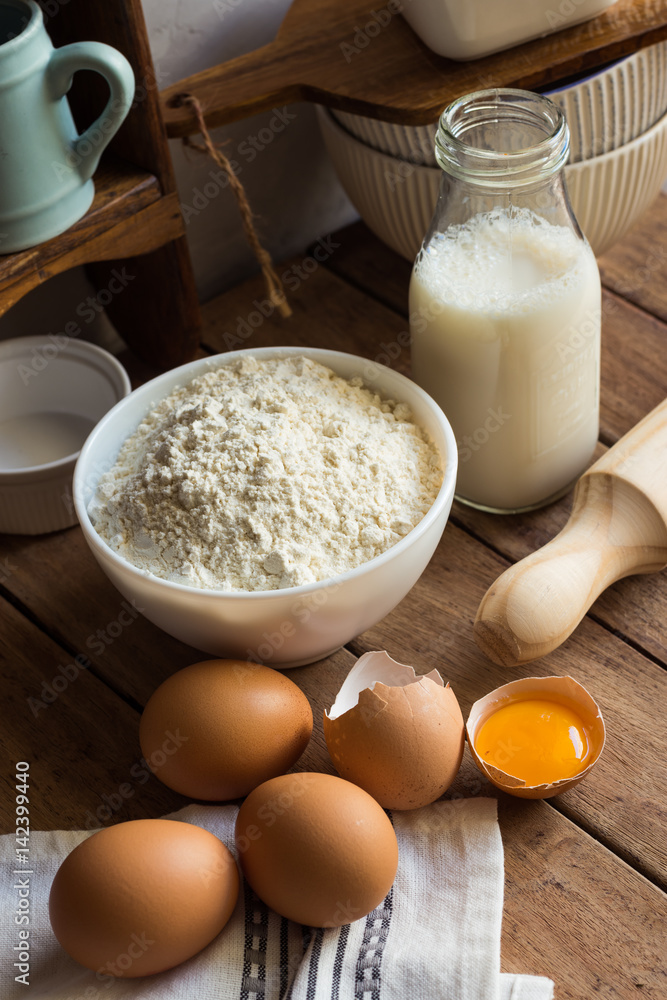 Baking ingredients flour, eggs, open yolk, milk, rolling pin, cupboard, rustic kitchen interior Baking ingredients flour, eggs, open yolk, milk, rolling pin, cupboard, rustic kitchen interior