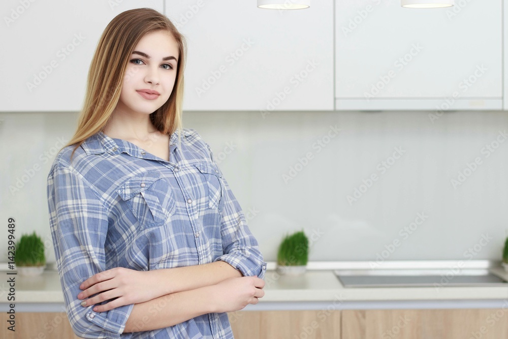 Young beautiful girl in a blue checkered shirt and blue jeans stands in the kitchen. Home interior