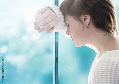 Sad woman grief leaning against a window
