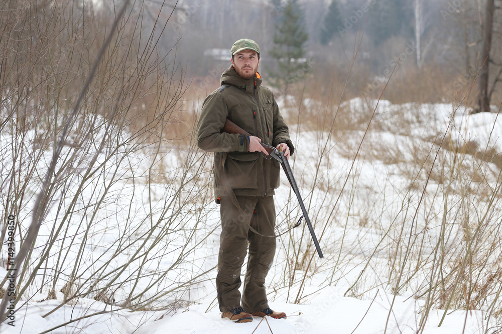 Hunter man with shotgun dressed in dark khaki clothing in the forest