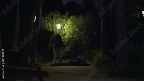 Murder on a dark urban park at night slomo.A man holding a knife flees the scene after the murder of another man on a dark park at night. photo