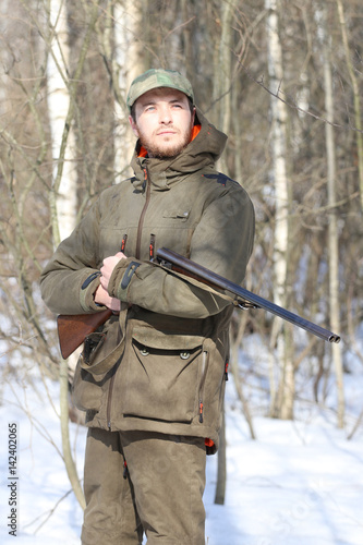 Hunter man with shotgun dressed in dark khaki clothing in the forest
