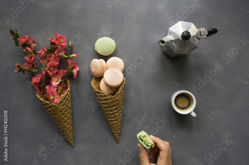 Coffee, macarons and flowers in ice cream cone on cement background