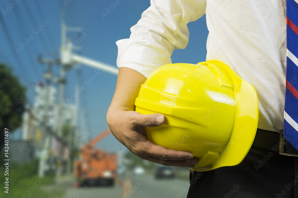 engineer or worker hold in hand yellow helmet ,Engineer and worker discussing blueprint next to electrical substation for workers security in front of construction blur background. Selective focus. engineer or worker hold in hand yellow helmet ,Engineer and worker discussing blueprint next to electrical substation for workers security in front of construction blur background. Selective focus.