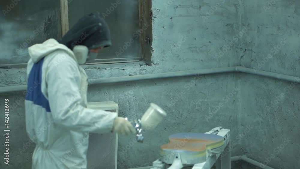 Man in protective suit atomizes paint layer on a guitar