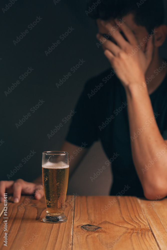 Concept of alcoholism. Sad man at the table with a glass of beer in a dark room.