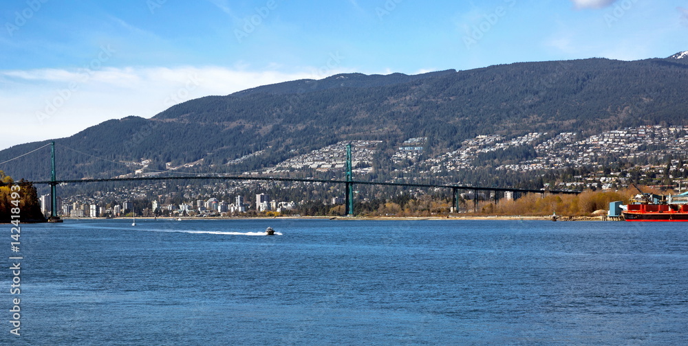 Lion Gate Bridge and City by the Sea, a motor boat going under the bridge on the background of mountain landscapes