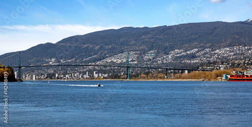 Lion Gate Bridge and City by the Sea, a motor boat going under the bridge on the background of mountain landscapes © Alex Lyubar