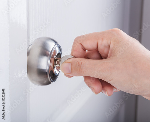 Hand use the key for unlocking door knob on white door