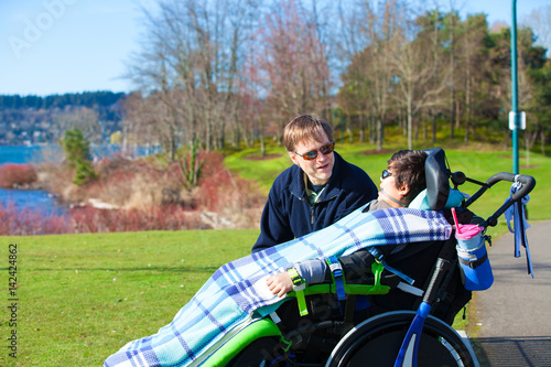 Disabled boy in wheelchair talking with father at lakeside park