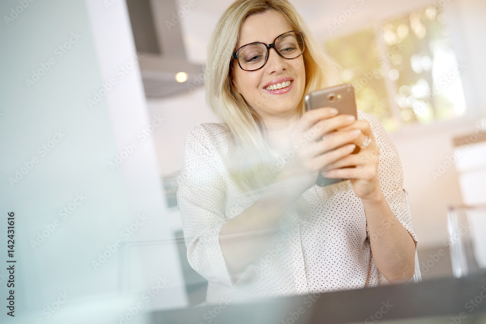 Blond woman with eyeglasses connected on smartphone at home Blond woman with eyeglasses connected on smartphone at home
