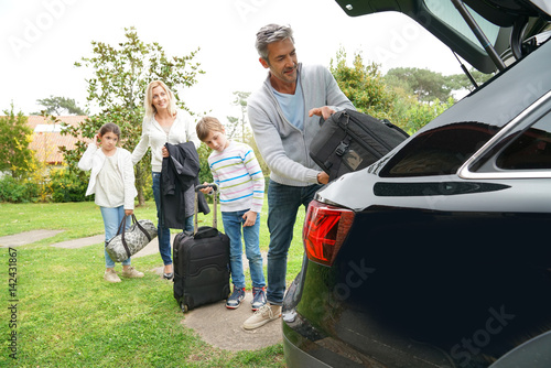 Family of four loading car trunk to leave for vacation
