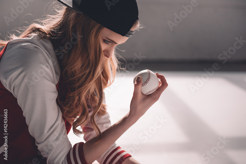 Photography Side view of young sporty woman in cap holding baseball ball