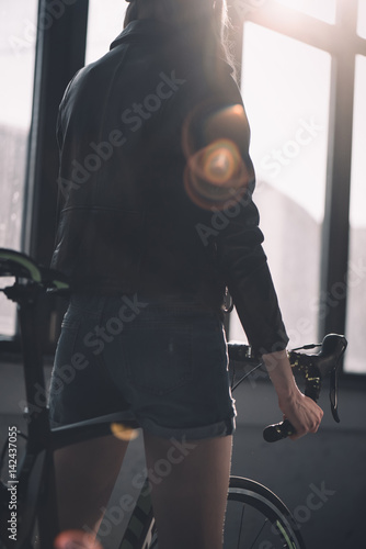 back view of young stylish woman riding bicycle
