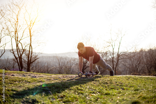 Man in nature doing push up with weights