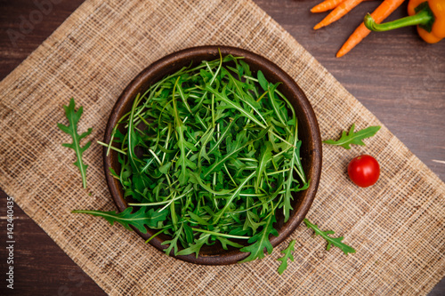 Arugula leaves in bowl. Fresh salad. Carrot, pepper and cherry tomatoes. Natural raw vegetables. Organic bio food on rustic wooden table.