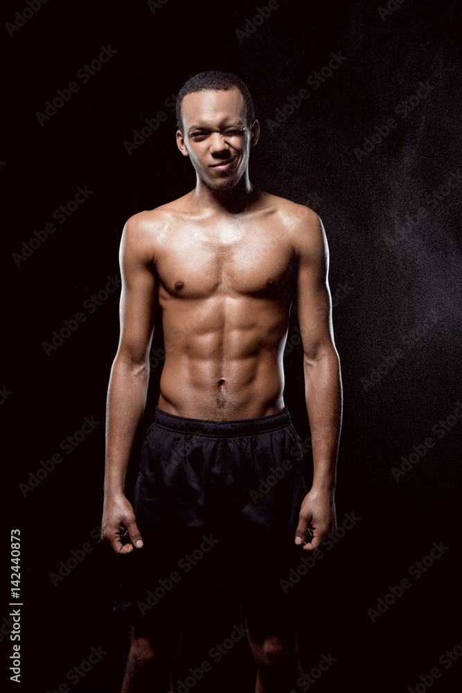 African american muscular man blinking and posing on black