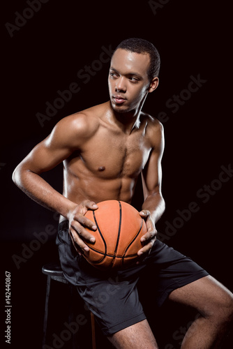 African american basketball player posing with ball on black