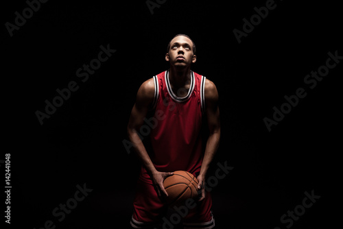 african sporty man in sports uniform playing basketball on black