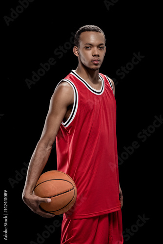 Young confident basketball player standing with ball and looking at camera