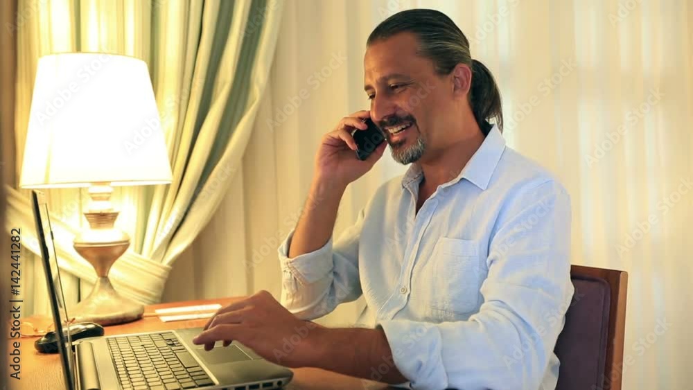 middle age attractive handsome man using laptop and talking on smartphone middle age attractive handsome man using laptop and talking on smartphone