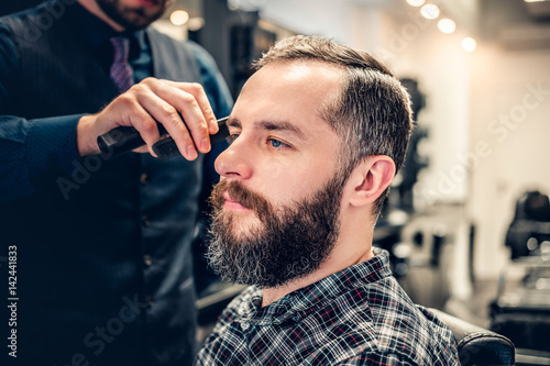 Hairdresser doing haircut to a bearded man in a barbershop.