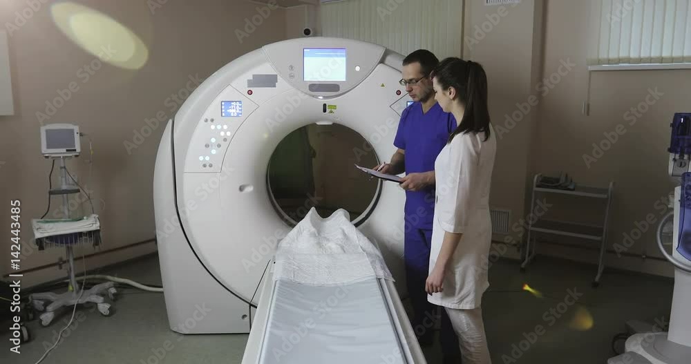 4K Two doctors discuss the patient's medical history in the CT scan room in a new modern cancer treatment hospital. 4K Two doctors discuss the patient's medical history in the CT scan room in a new modern cancer treatment hospital.