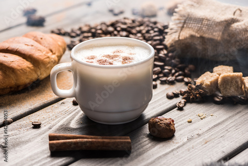 close up view of cup of coffee with cinnamon sticks and cookies on table