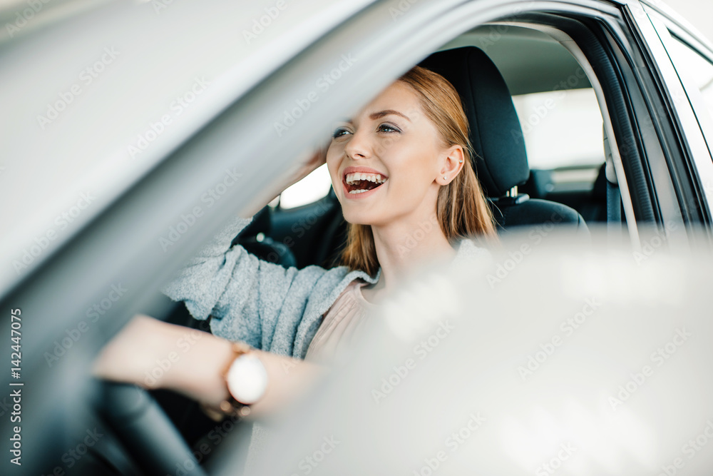 Happy beautiful young woman driver sitting in new car