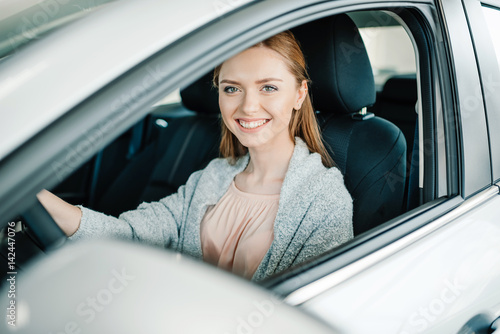 Happy beautiful young woman driver sitting in new car