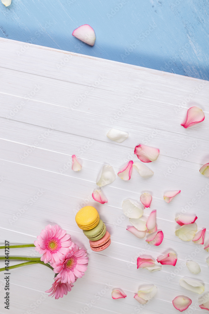 Macaroon cakes with pink rose petals and Gerbera flowers. Different types of macaron. Colorful almond cookies. On white wooden rustic background. Macaroon cakes with pink rose petals and Gerbera flowers. Different types of macaron. Colorful almond cookies. On white wooden rustic background.