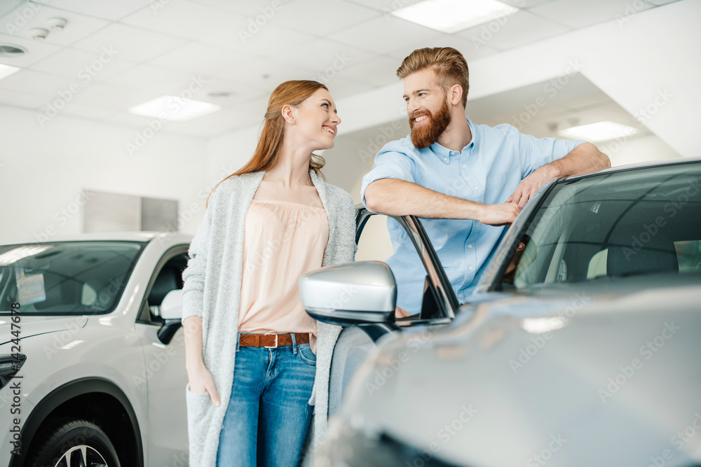 Happy young couple standing near new car and smiling each other Happy young couple standing near new car and smiling each other