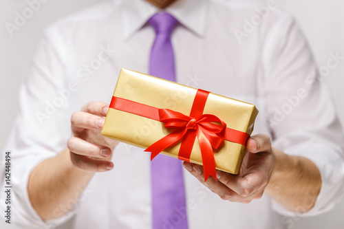 Male hands holding a gift box. Present wrapped with ribbon and bow. Christmas or birthday package. Man in white shirt and necktie. © tanyastock