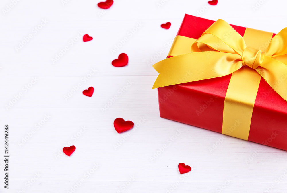 Gift box with red satin hearts. Present wrapped with yellow ribbon. Christmas or birthday package. On white wooden table. Gift box with red satin hearts. Present wrapped with yellow ribbon. Christmas or birthday package. On white wooden table.