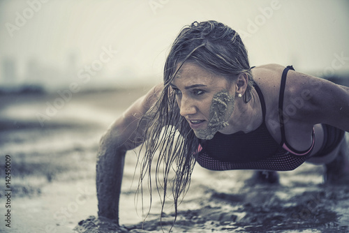Strong athletic woman laughing with mud on her face crawling in mud or extreme sport with with grungy texture 