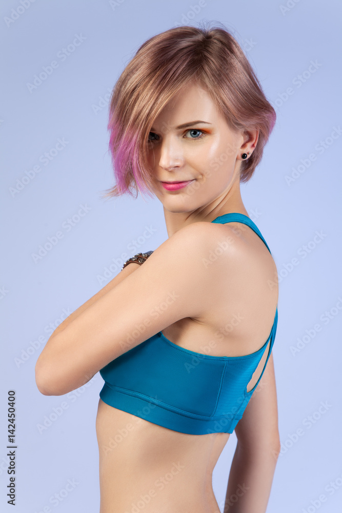 Studio portrait of a young girl with a colored strand of hair in the sports top, isolated on a blue background Studio portrait of a young girl with a colored strand of hair in the sports top, isolated on a blue background