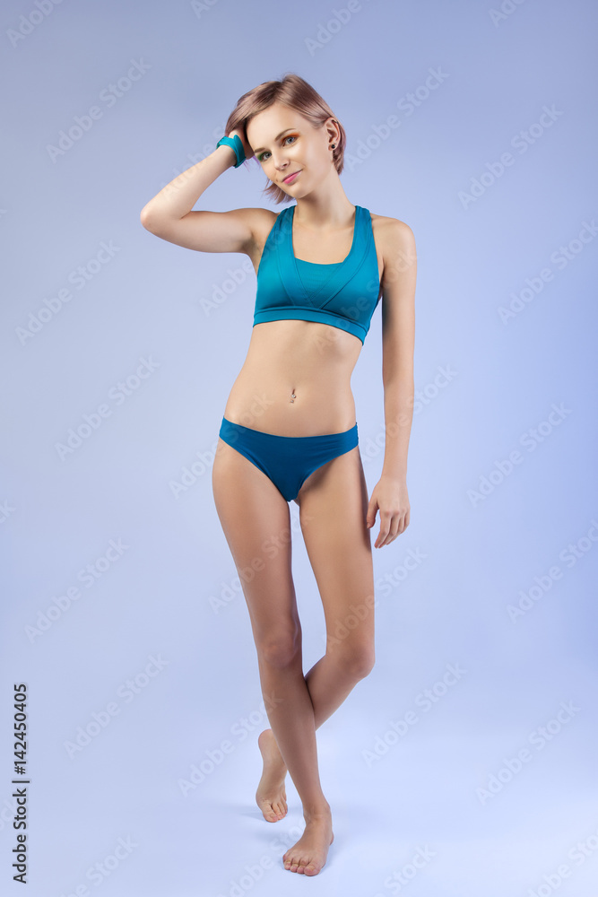 Foto de Studio portrait of a young girl in a sports underwear in full  growth isolated on a blue background do Stock