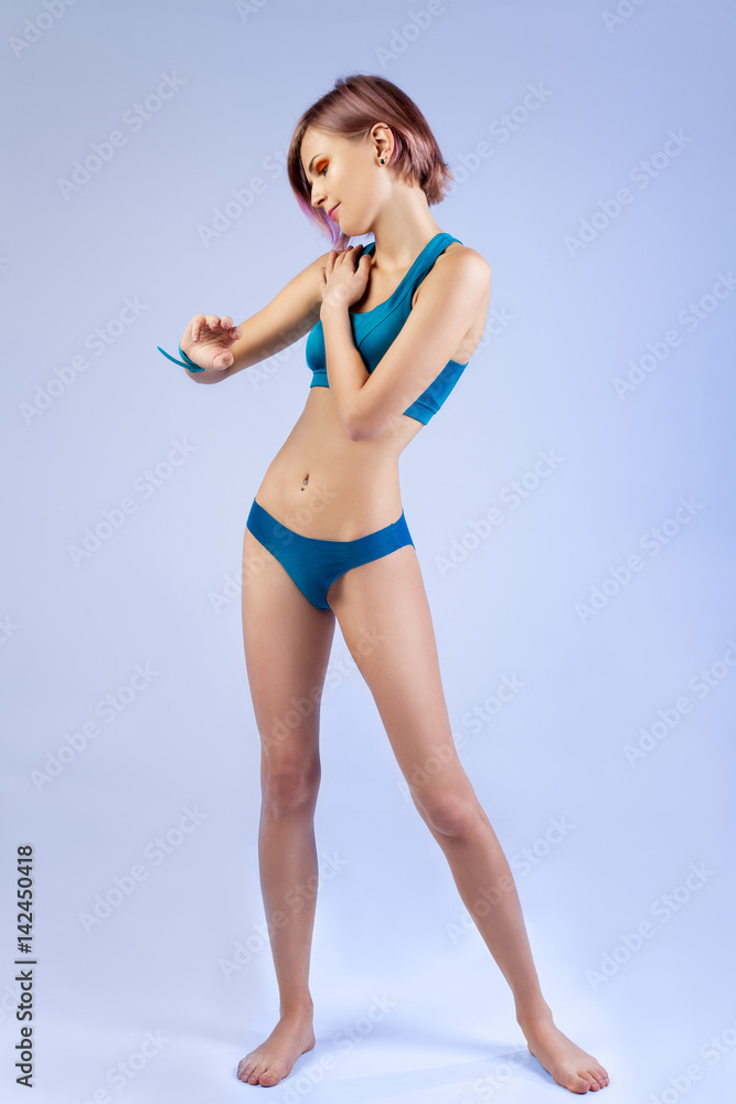 Young thin girl in a sports underwear in full growth looking at her watch,  isolated on a blue background Stock-foto