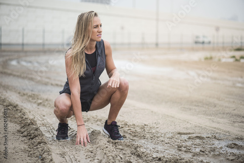 A beautiful strong athletic woman crouching down on a muddy ground before starting her run.