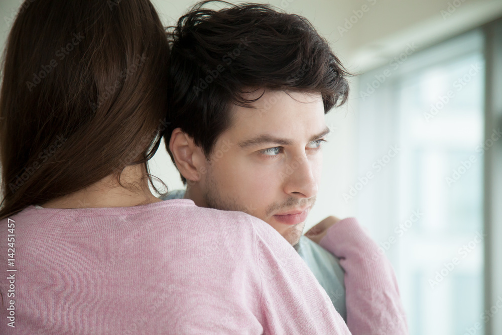 Woman hugging her upset boyfriend, sad guy looking away through the window, loving wife supporting husband, embracing and comforting him, helping to solve business problems, couple reconciliation Woman hugging her upset boyfriend, sad guy looking away through the window, loving wife supporting husband, embracing and comforting him, helping to solve business problems, couple reconciliation