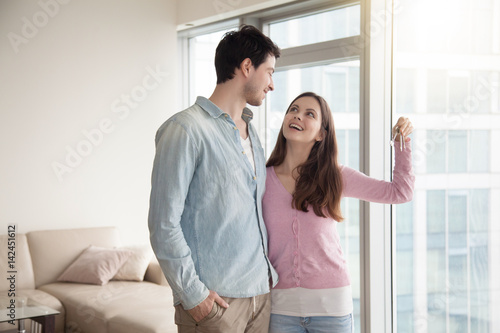 Young smiling couple holding and showing keys of their new own home, happy family buying or renting house or apartment, paid real estate mortgage, teenagers left parental home, starting married life
