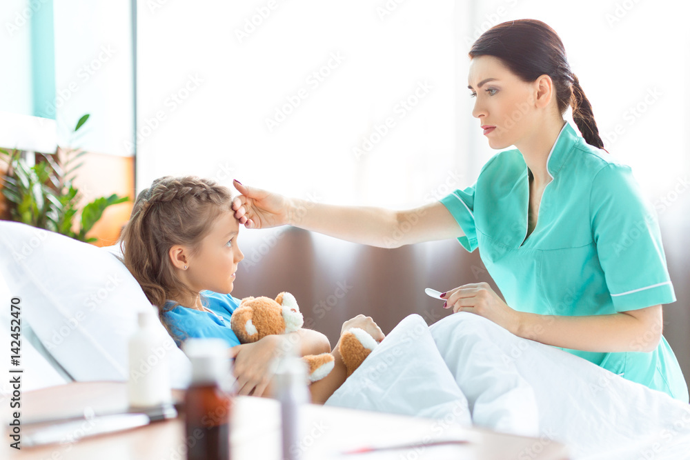 Side view of nurse checking temperature of sick little girl in hospital bed Side view of nurse checking temperature of sick little girl in hospital bed
