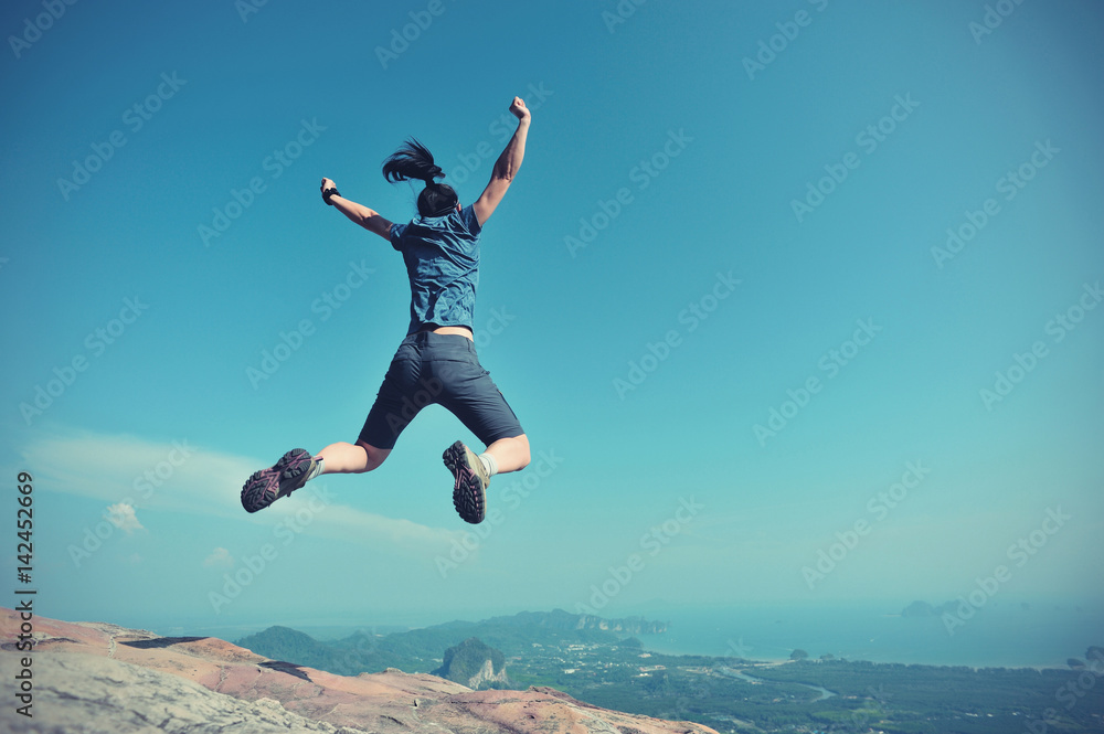 successful woman jumping on rocky mountain peak, freedom, risk, challenge, success concept