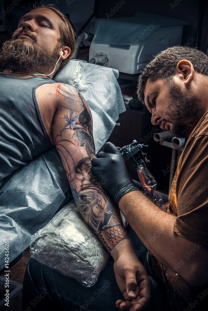 Fototapeta premium Tattoo master showing process of making a tattoo in tattoo parlor